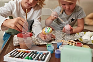 Close up of hands of adorable little boy painting colorful Easter eggs together wih his sister while spending time at
