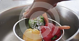 Close up of hands of african american woman rinsing vegetables in kitchen sink, in slow motion