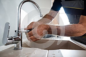 Close up of hands of aged repairman in uniform working, fixing broken kitchen tap using adjustable wrench. Repair