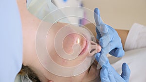 close-up. the hands of a beautician in rubber gloves apply cream to the face of a female patient