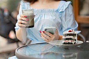Close up of hands beautiful woman reading news on her smartphone eating cake at outdoors cafe