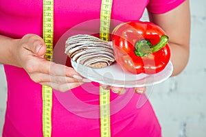 Close-up hands of a beautiful and young brunette woman holding a vegetable pepper and a plate of cookies and a measuring