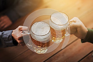 Close up of hands with beer mugs at bar or pub