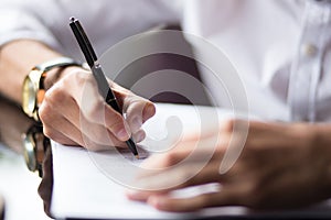 Close up of the hands of a businessman in a shirt signing or writing a document on a sheet of white paper using a nibbed