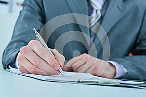 Close up of the hands of a businessman in a suit signing or writing a document on a sheet of white paper.