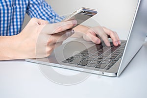 Close-up the hands of businessmen wearing a plaid shirt using mobile phones and laptop computers in the room