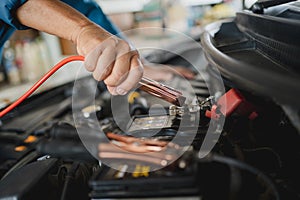 Close-up hands of a car mechanic holding the battery jumper wire. He uses battery jumper cables to charge a dead battery