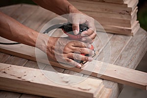 Close up Hands of carpenter equals polishes wooden board with a random orbit sander in the workshop