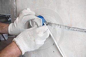 Close-up on the hands of a Caucasian male electrician installing a white AC outlet on a gray wall of a house.Home