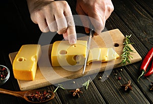 Close-up of hands the chef with a knife cut the cheese into small pieces for tasting on a cutting board. The concept of making