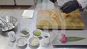 Close up hands of chef in white restaurant uniform cutting small salmon fish. Kitchenware around, spice, tunafish piece