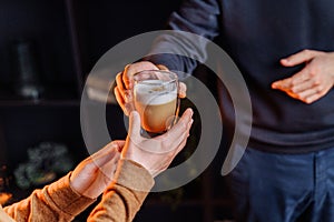 Close up of hands with coffee. Barman giving a freshly brewed, fragrant cappuccino with high milk froth in a transparent glass to