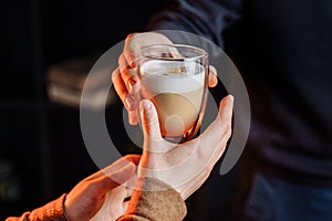 Close up of hands with coffee. Barman giving a freshly brewed  fragrant cappuccino with high milk froth in a transparent glass to