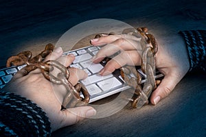 Close-up of hands, computer keyboard and old rusty chains on dark wooden background