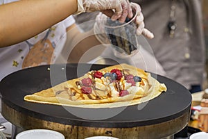 Close-up of hands of cook in gloves preparing Crepe, pancake on frying pan with fresh banana, blueberry, raspberry photo