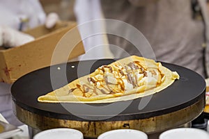 Close-up of hands of cook in gloves preparing Crepe, pancake on frying pan with fresh banana, sweet sauce, nutella photo