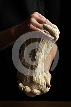 Close-up, the hands of the cook knead the dough on a black background, yeast sourdough