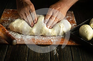 Close-up of the hands of the cook kneading the dough before baking the buns. Working environment on the kitchen table in the