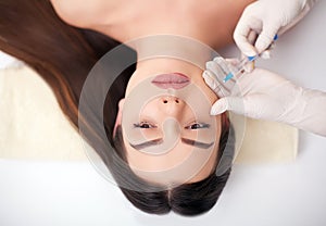 Close up of hands of cosmetologist making botox injection in female lips. She is holding syringe. The young beautiful woman is rec