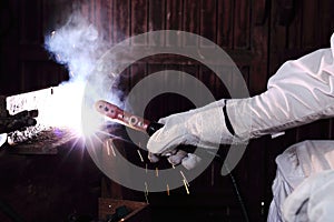 Close up hands of craftsman welder with torch and protective gloves welding metal steel with spark in the factory. Manufacturing i