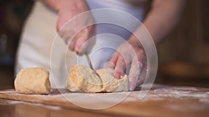 Close up hands cut shape in rolling-pin dough into pieces on wooden board covered with flour