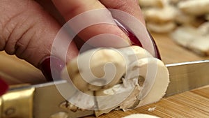 Close-up of the hands cutting fresh champignons into slices on the wooden board
