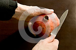 Close-up of hands cutting open a pomegranate with a stainless steel knife - dark background