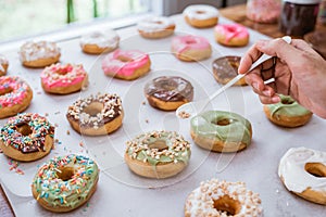 Close up of hands decorating various donuts with chocolate frosted, pink glazed and donut sprinkle