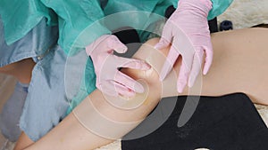 Close-up of the hands of a doctor in medical gloves who rubs ointment into the damaged part of the patient's knee.