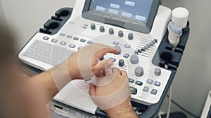 Close-up hands of doctor works on ultrasound scanner. Medical worker use special equipment.