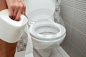 Close-up, hands duvushki, holding a roll of toilet paper in front of the toilet. The concept of problems with the intestines,