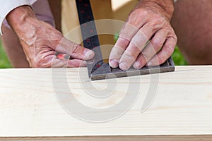 Close-up of the hands of an elderly craftsman - carpenter at work holding a metal ruler and a graphic pencil drawing markings on a