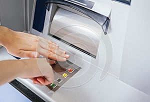 Close-up of hands entering and hiding PIN number password code on ATM bank machine key pad. Secure banking operations and habits