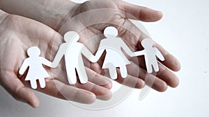 Close up hands of father, mother and daughters protecting family paper cutout.