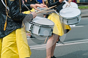 Close-up of hands of female drummers in yellow black vintage uniform at parade. Street performance. Parade of majorettes