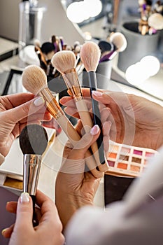 Close up hands of female makeup artist studying client choosing brush for cosmetics applying