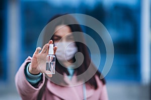 Close up hands of female in medical mask cleaning her hands with sanitizer outdoor in the city to prevent virus deseases.