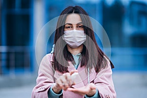 Close up hands of female in medical mask cleaning her hands with sanitizer outdoor in the city to prevent virus deseases.