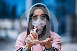 Close up hands of female in medical mask cleaning her hands with sanitizer outdoor in the city to prevent virus deseases.