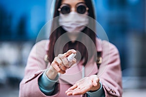 Close up hands of female in medical mask cleaning her hands with sanitizer outdoor in the city to prevent virus deseases.