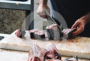 Close up hands of fisherman cutting tuna with a huge cleaver on a wooden board. Blurred tuna meat in the foreground. Local fish