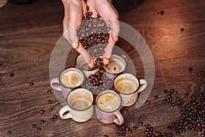 Close-up of the hands of a girl who sprinkles roasted coffee beans to the floor. On the floor there are cups of freshly brewed