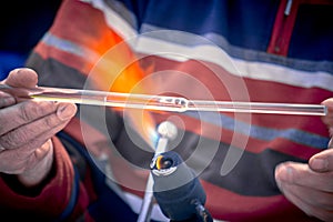 Close-up of the hands of a glassblower working on a glass object.