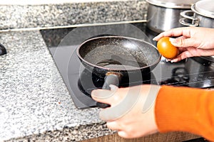 close-up of hands going to break an egg to fry it in a frying pan on induction cooker photo