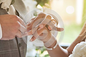 Close up hands of groom holding hands bride and putting wedding ring on finger fiancee