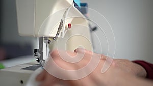 Close up of Hands of Hardworking European Elderly Woman, stitching fabric using Sewing Machine at her Workshop, Focused