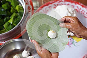 Close up hands hold banana leaf to wrap dough bun for cooking Thai traditional dessert.