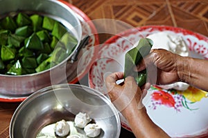 Close up hands hold banana leaf to wrap dough bun for cooking Thai traditional dessert.