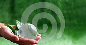 Close up of hands holding crystal globe on green grass with blur nature background, earth day or world environment day concept.