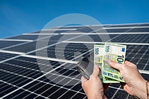 close-up of hands holding euro money in wallet over solar panels on their background.